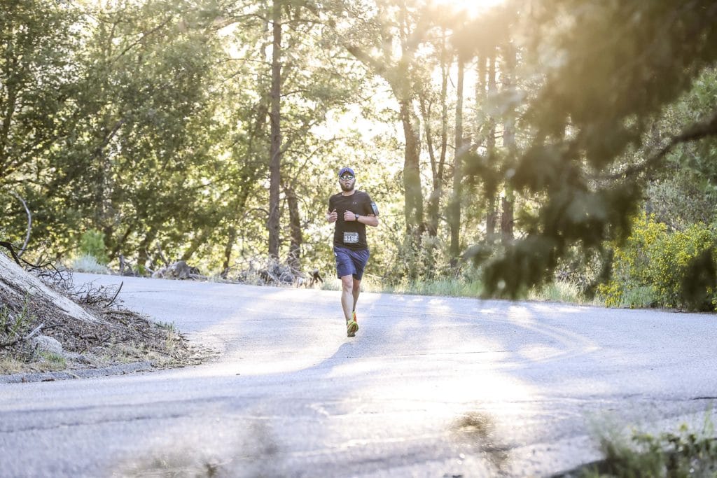 A man running on a wide paved road in the forest with light shining around him