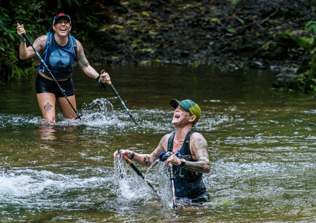 Two women trekking through water with poles and laughing