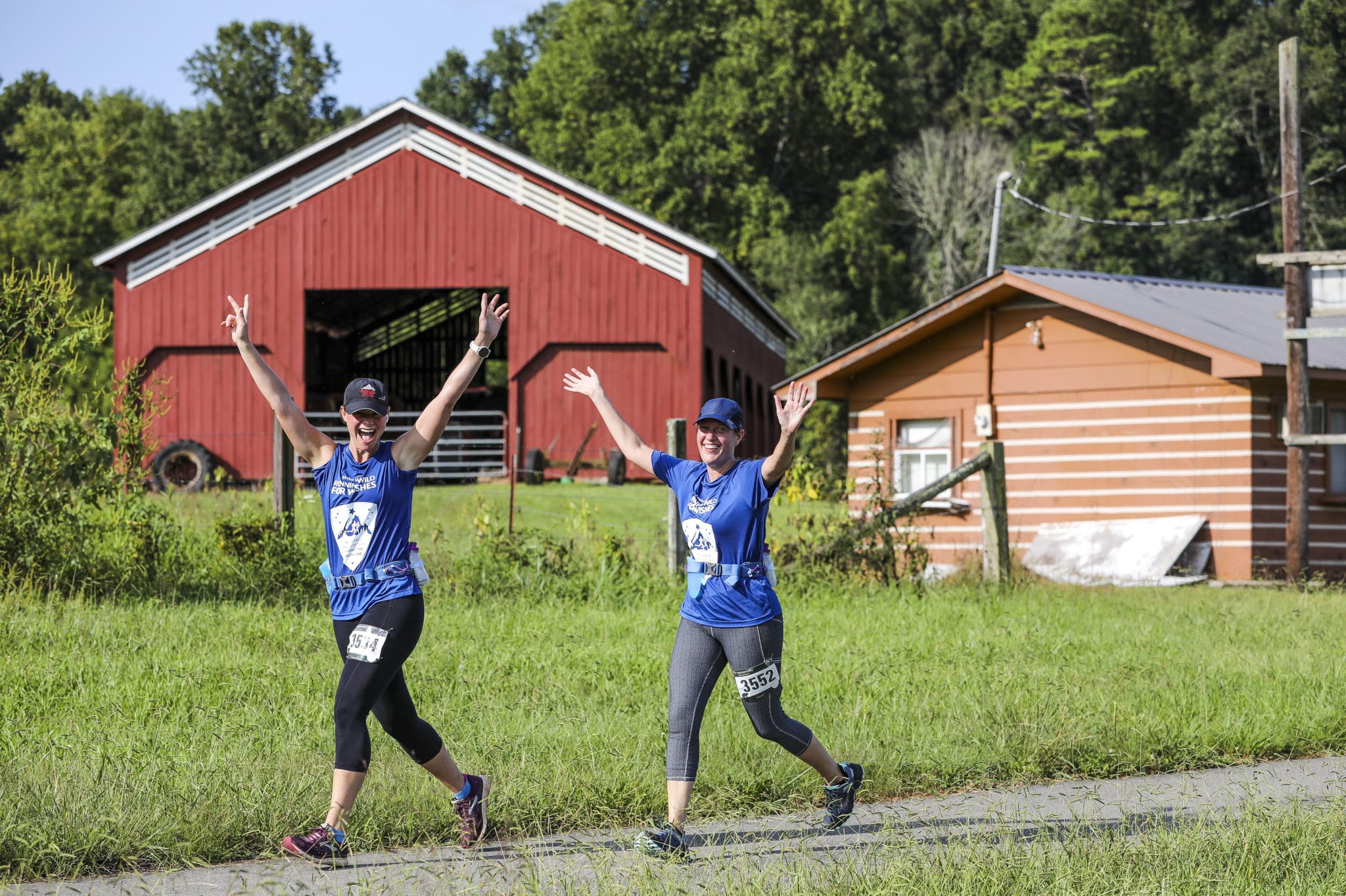 Two young woman running past a sunny field and barn