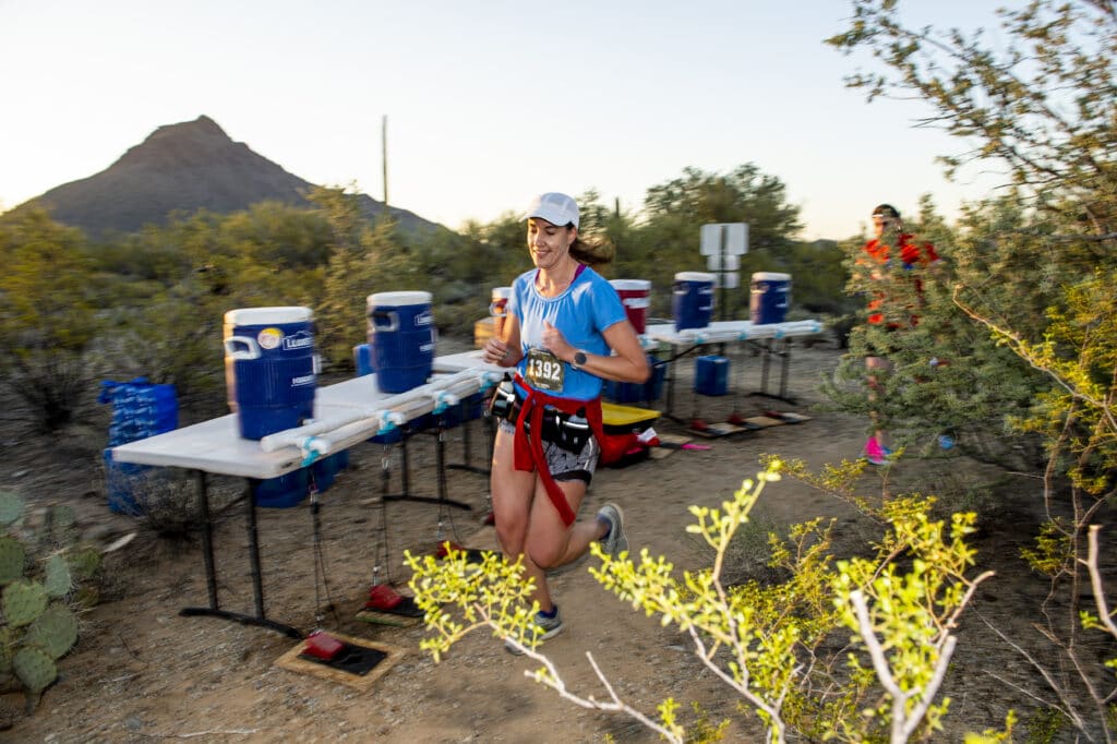 woman jogging past aid station with water and Gnarly Hydrate coolers