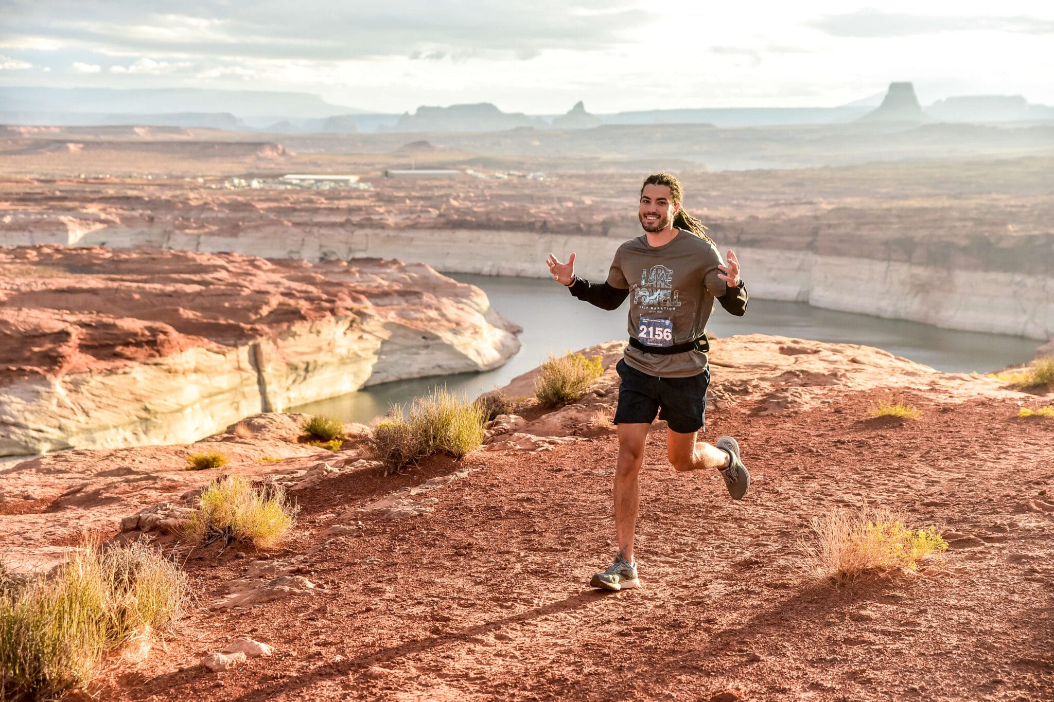 man smiling and running on a dirt trail past lake powell