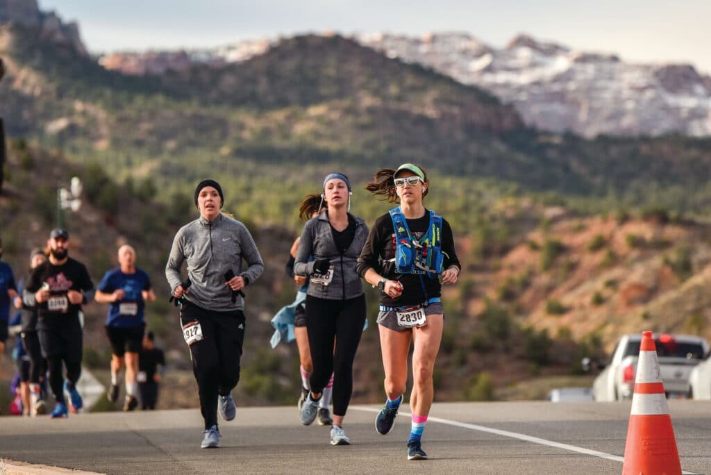 Group of runners running up a hill with mountains behind them