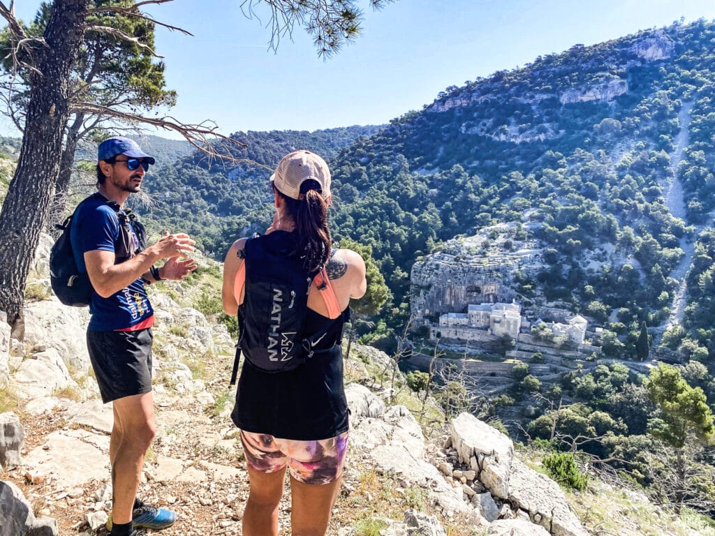 Two runners looking out over a canyon with stone ruins in the cliffside