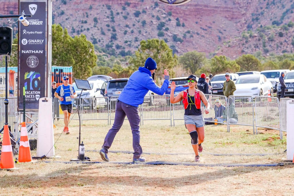 A runner crossing the finish line and getting high fived be the race announcer