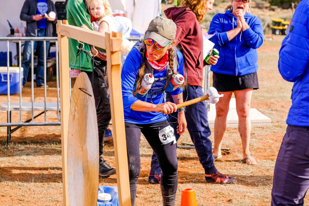 A finisher ringing the finish line gong covered in dust and dirt from the trail