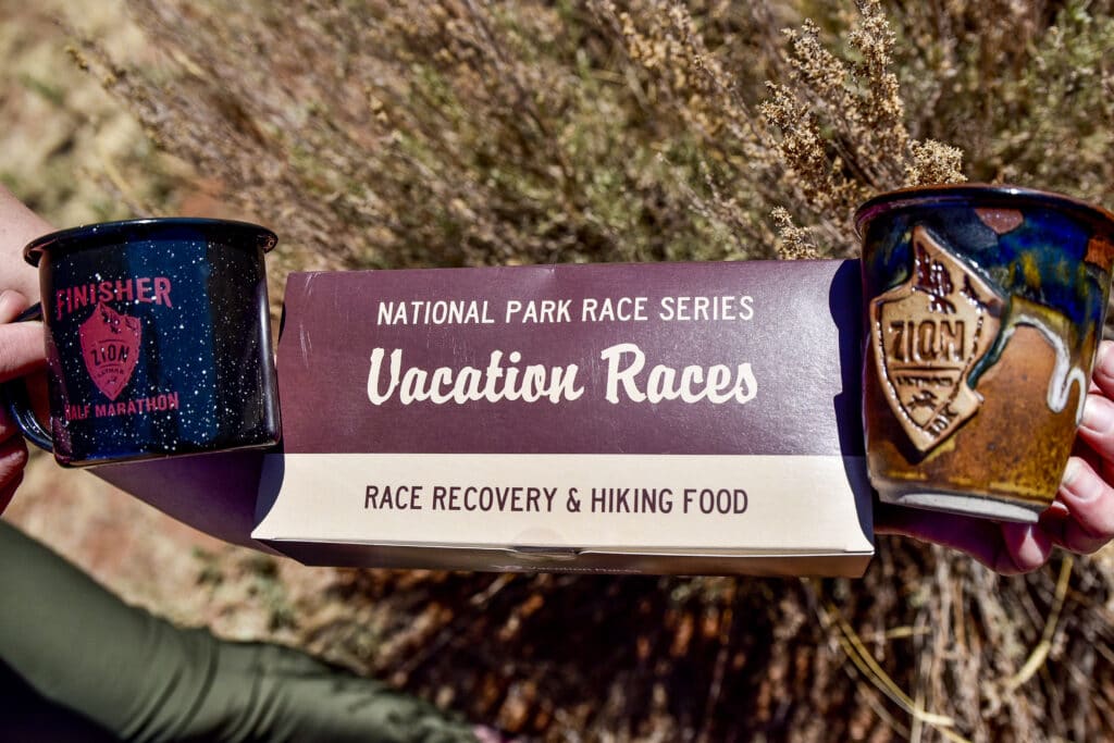 a runner recovery box full of snacks next to two finisher prize ceramic cups