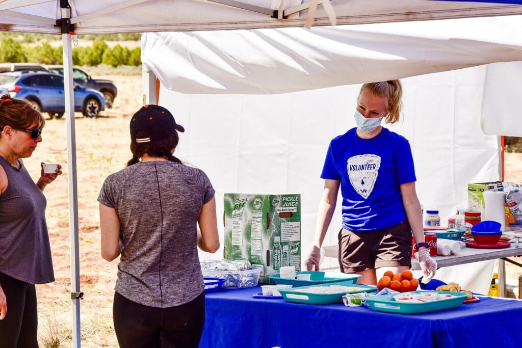 aid station worker in a face mask behind a table of fresh cut fruit