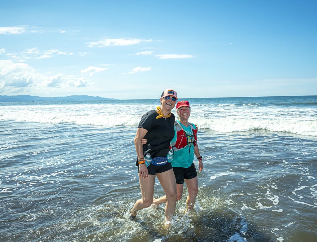 A mother and daughter embrace while they walk along the shoreline
