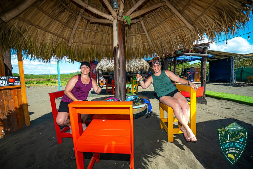 Two running sitting under a straw umbrella with drinks
