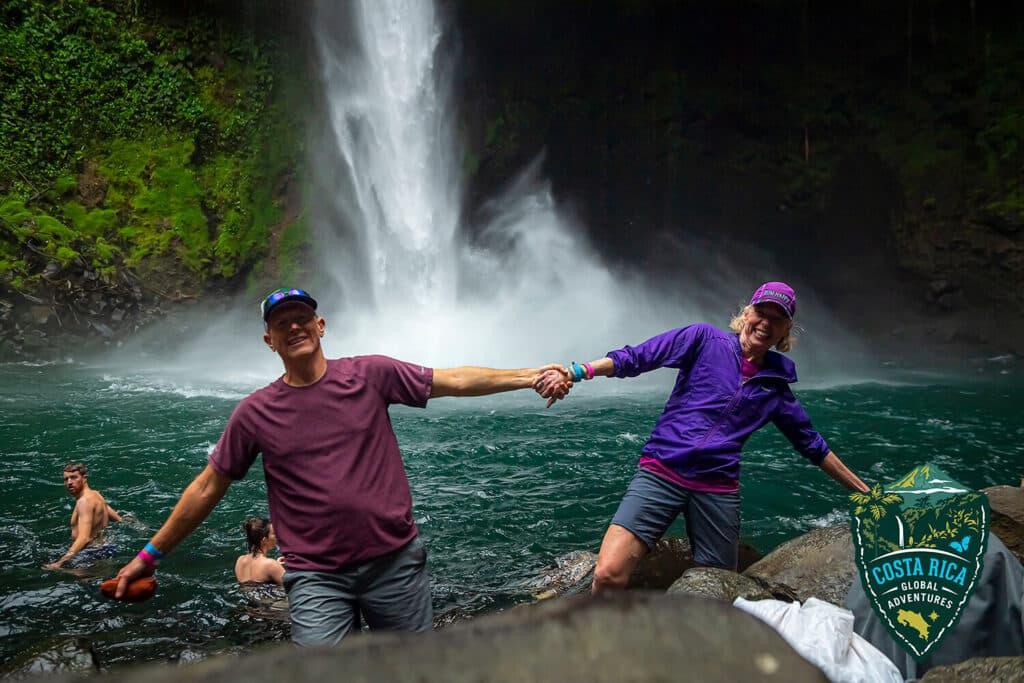 A couple hold hands in front of a waterfall