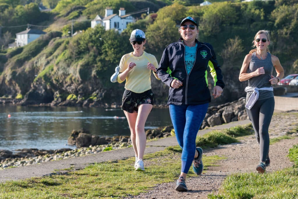 a group of people running along a dirt trail with a bay behind them