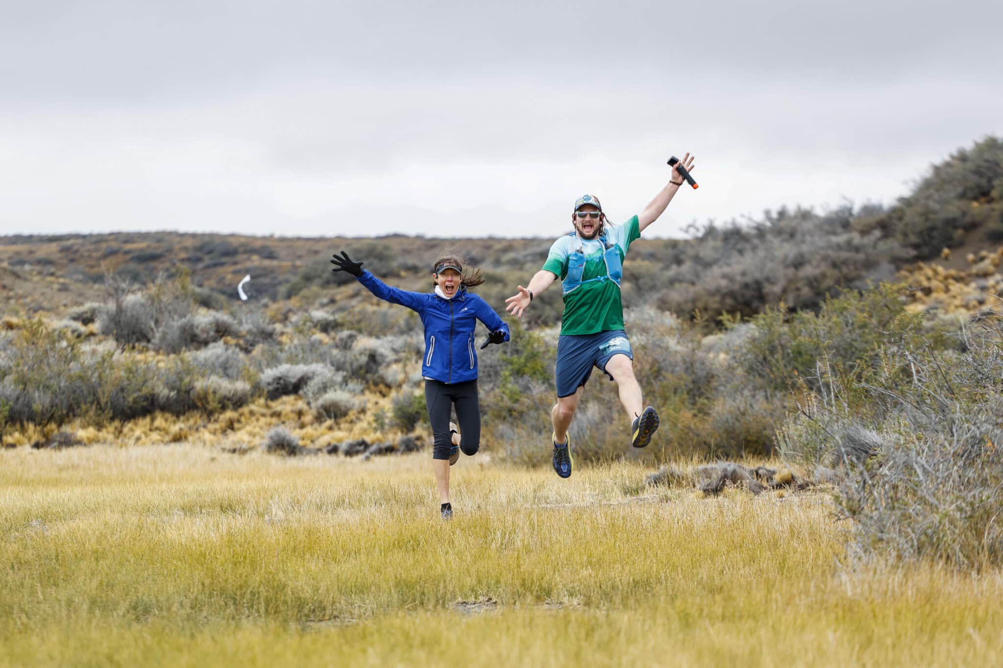 Patagonia_DIA 2 VRGA - LA LEONA-006 two running jumping into the air with greenery and brush behind them
