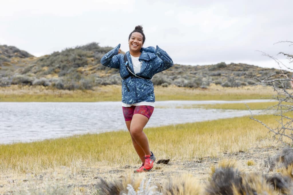 young woman smiling and giving thumbs up as she runs along a marsh