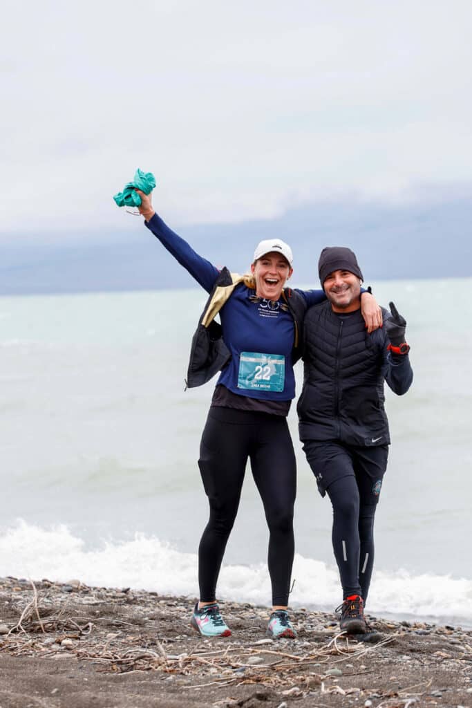 two adults with their arms around each other walking with water behind them