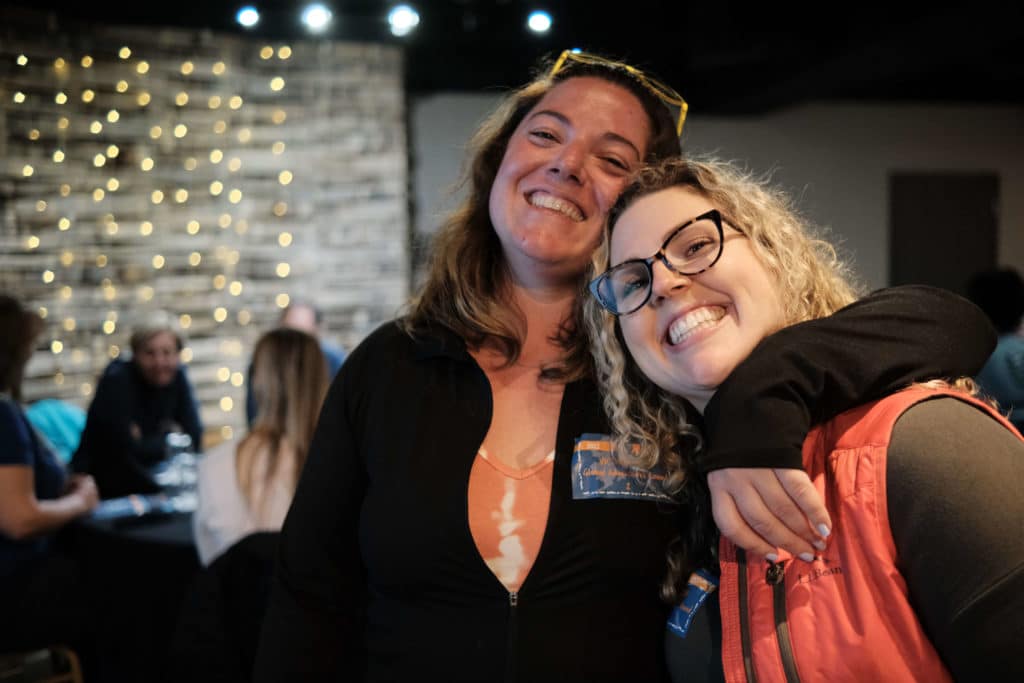Two friends smile at the camera and lean into each other at the welcome dinner