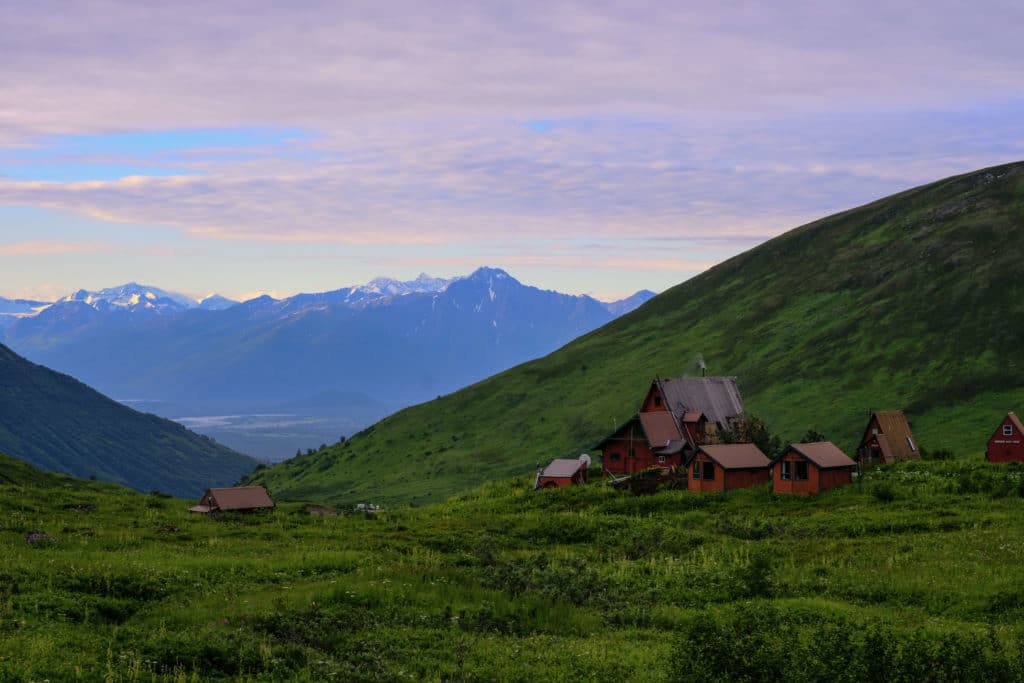 The sunset landscape of Hatcher Pass with vibrant green valleys and old abandoned wooden buildings in the distance