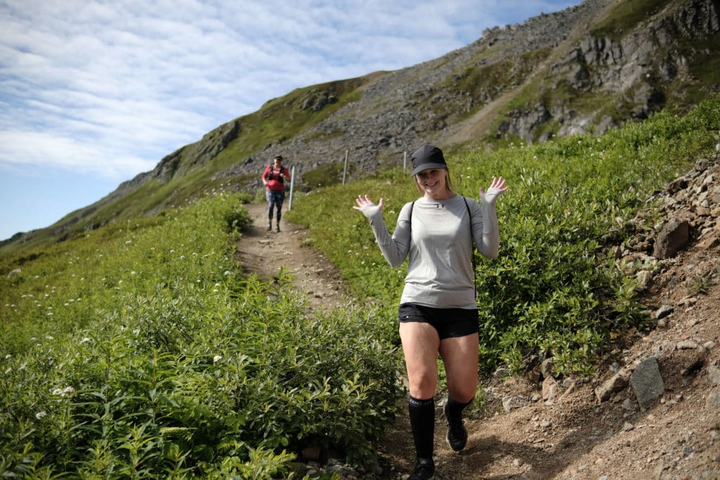 A woman raises her hands as she descends a grassy slope
