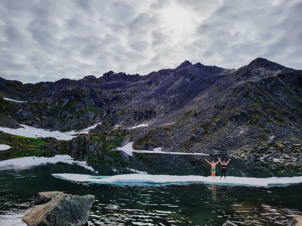 Two runners stand proudly on a floating slab of ice in a rocky mountain lake after a run
