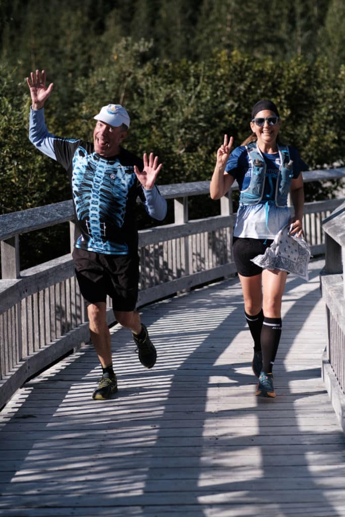 Two runners make silly faces as they round a bend in a wooden bridge