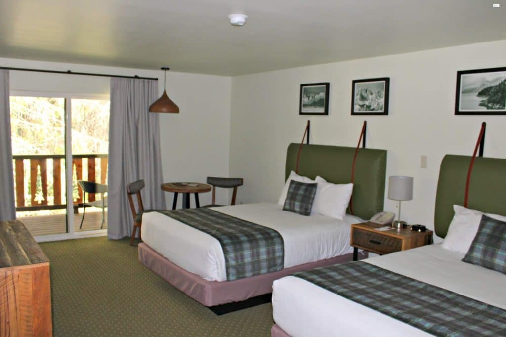A green and white double hotel room with leather and wood accents and green tartan blankets