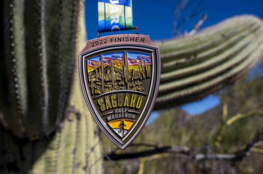 2022 Saguaro medal hanging on a zsaguaro cactus with the sun shining down on it