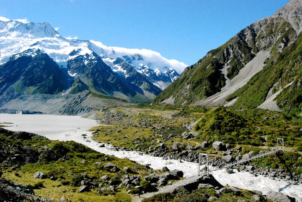 A valley a glacial stream stretches towards a vast and imposing snowcapped mountain range