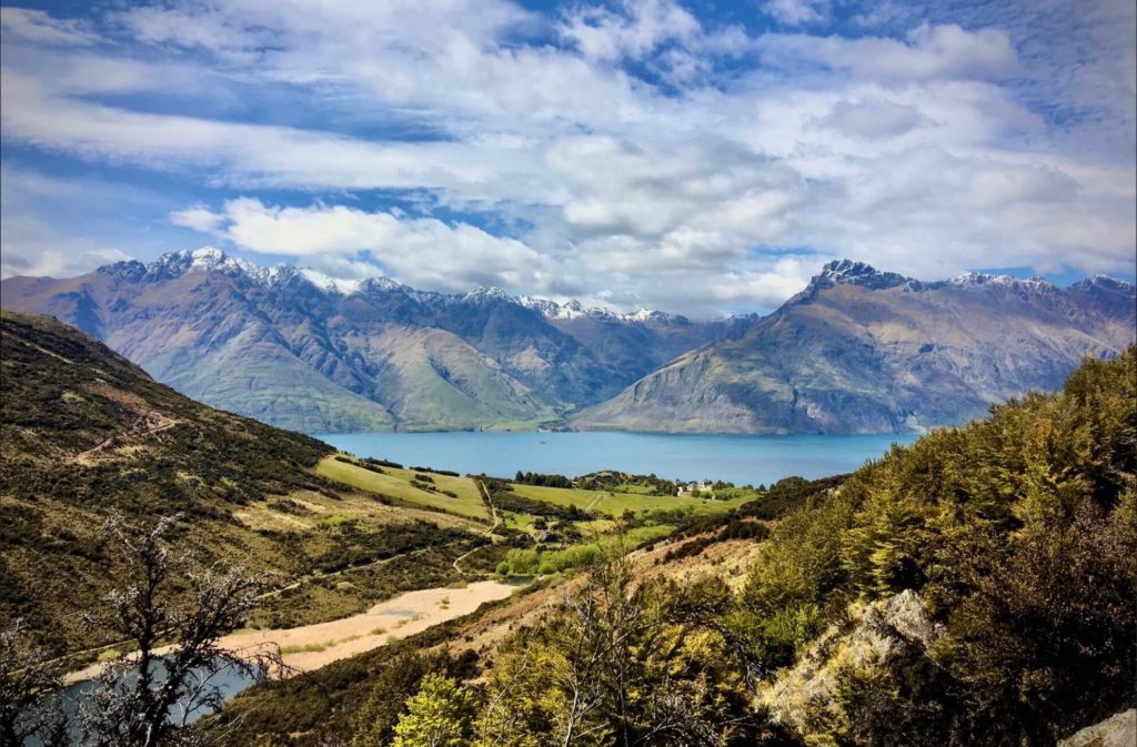 A green valley empties out into turquoise waters backed by the wide peaks of New Zealand