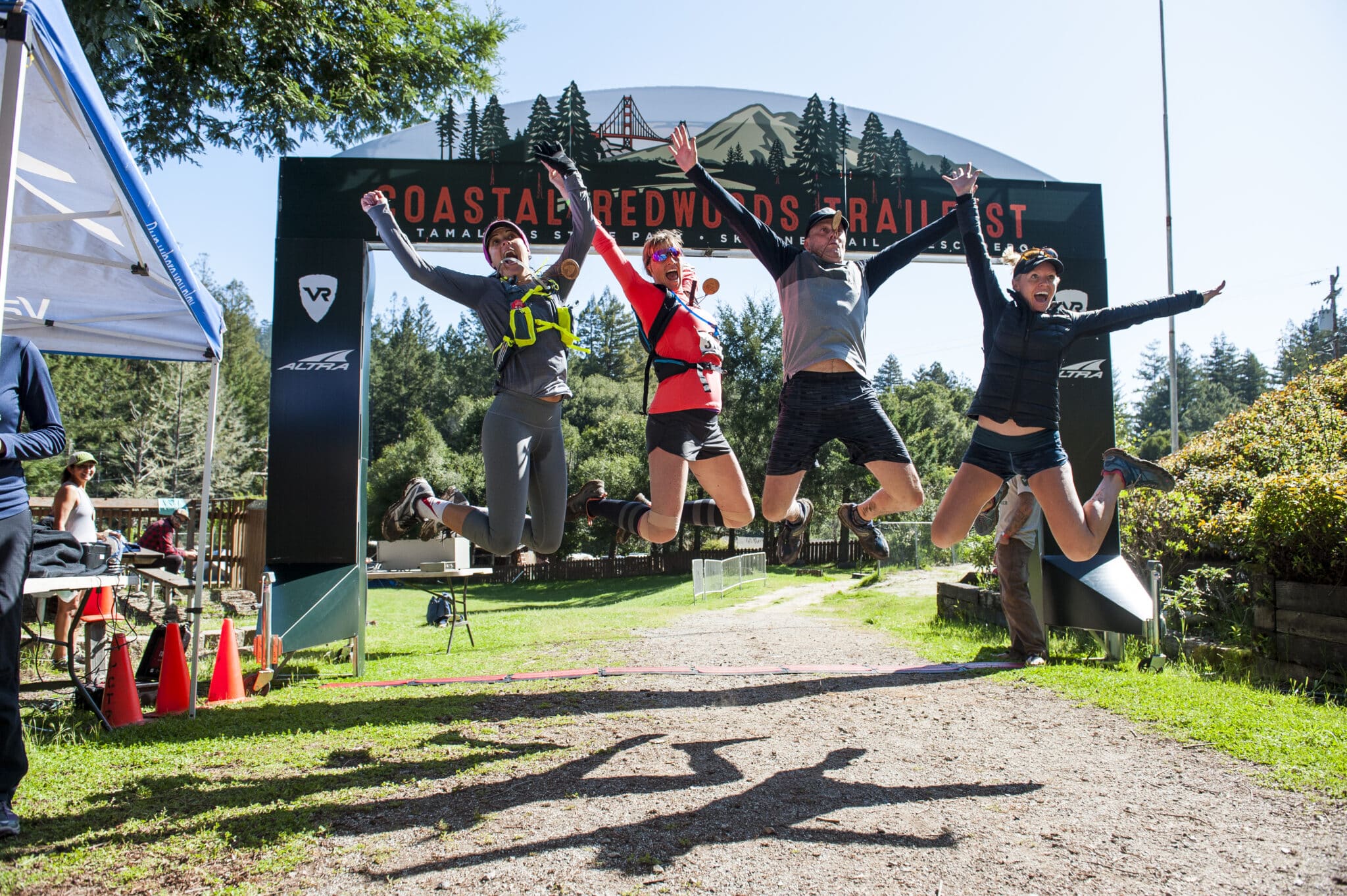 Vacation races runners jumping for joy in front of the Coastal redwoods finish line