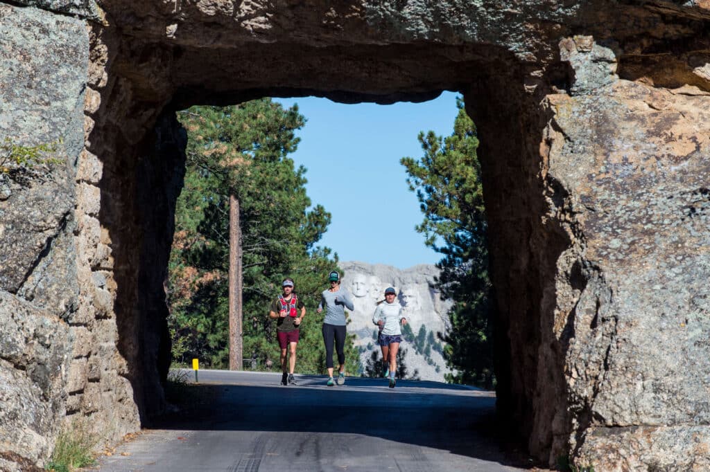 Three Vacation Races runners entering the tunnel with Mount Rushmore behind them