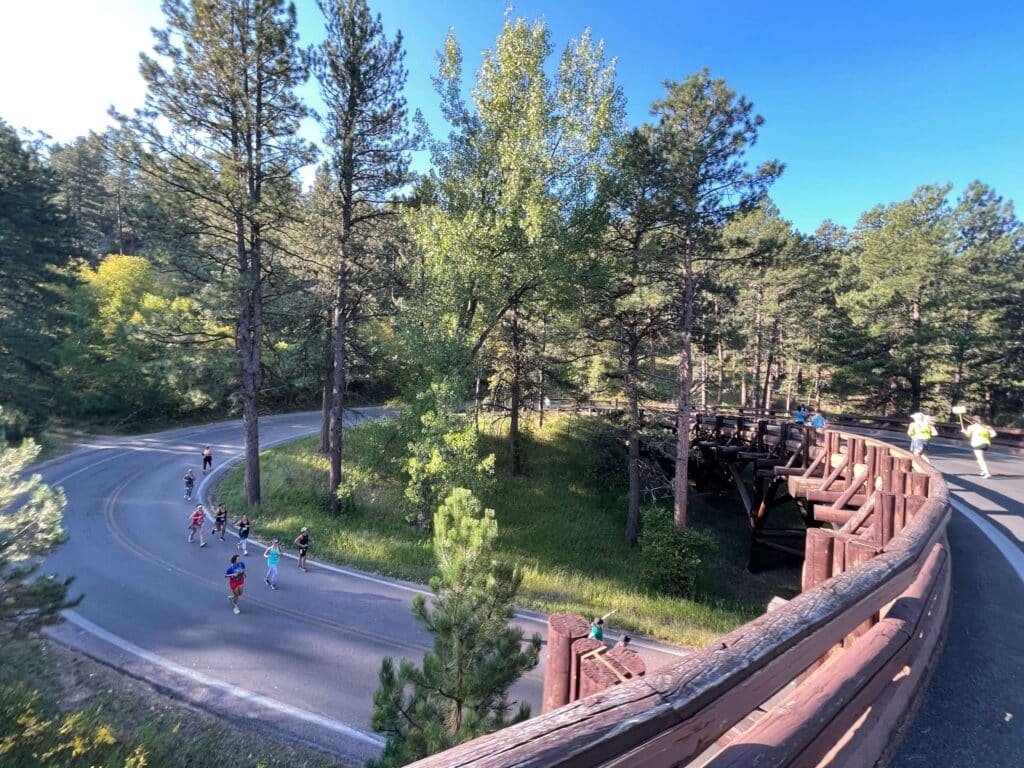 View of half marathon runners running through trees in the Black Hills at the Vacation Races Mount Rushmore Half Marathon