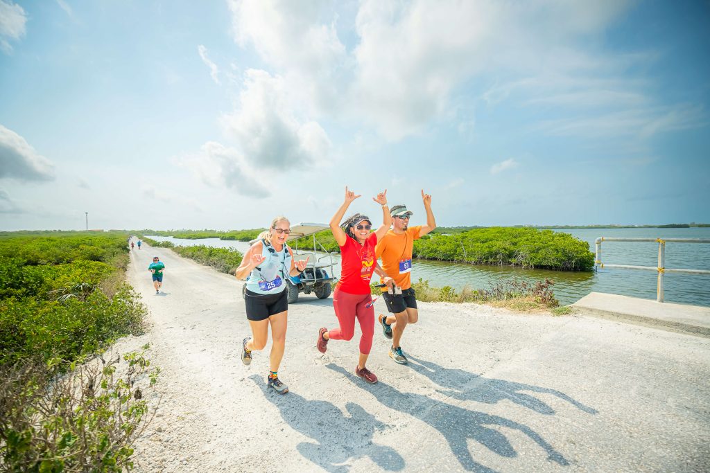Three runners cheer as they run along the water on Ambergris Caye in Belize attheir all-inclusive running trip