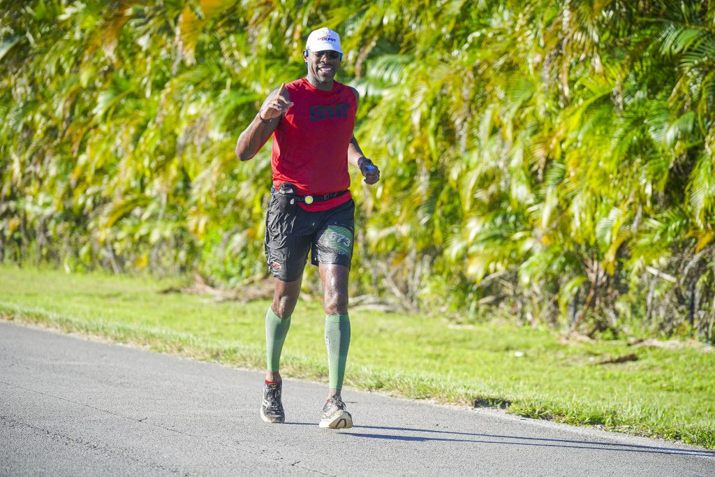 A lone runner wearing a Black Men Run shirt strides past lush greenery on the Everglades Half Marathon course