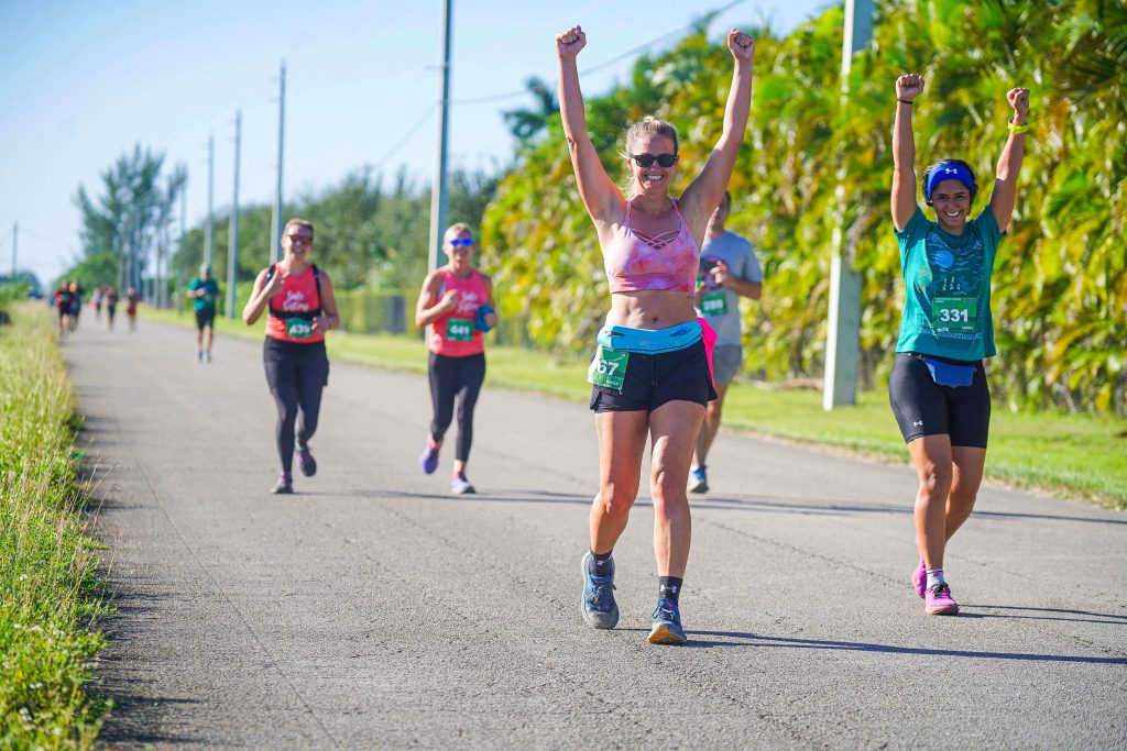 A group of Vacation Races women in matching shirts yell and wave their arms as they run the Everglades Half Marathon