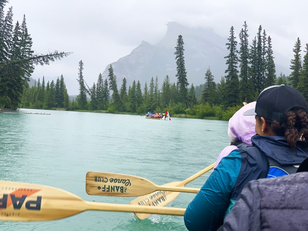 A group of people paddling their canoe through aqua waters with peaks and evergreen trees on either side