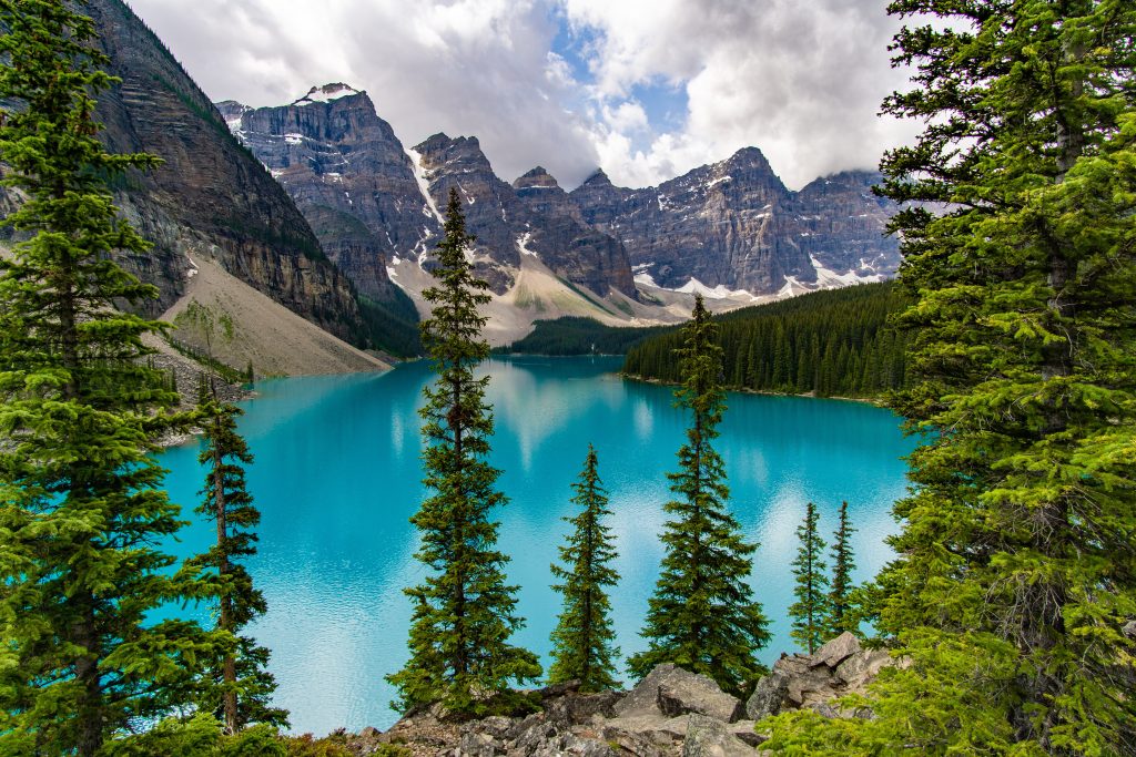Turquoise still waters are framed by stone mountains with teetering pine trees in the foreground