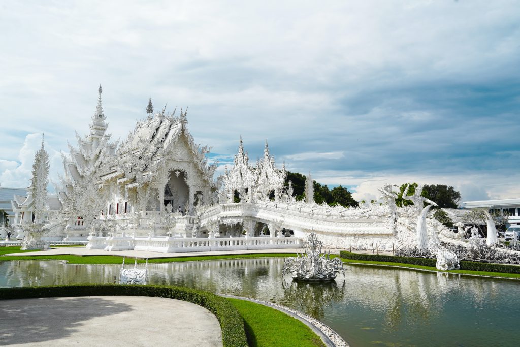 White temple of Wat Rong Khun with a serene lake in front