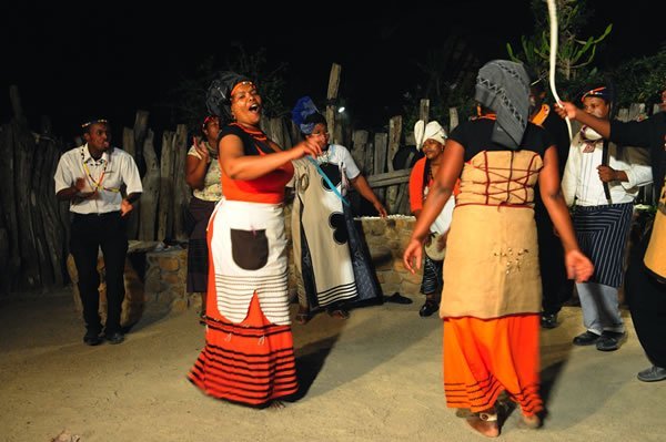 Dancers wearing vibrant red and gold sing and perform at a nighttime show